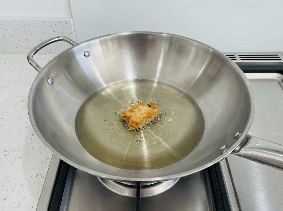 A piece of breaded chicken frying in a wok filled with hot oil.