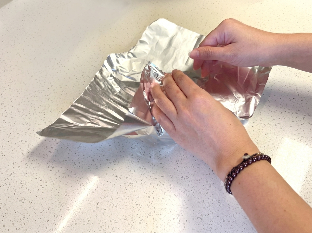 Hamburger buns being wrapped in individual squares of aluminum foil.