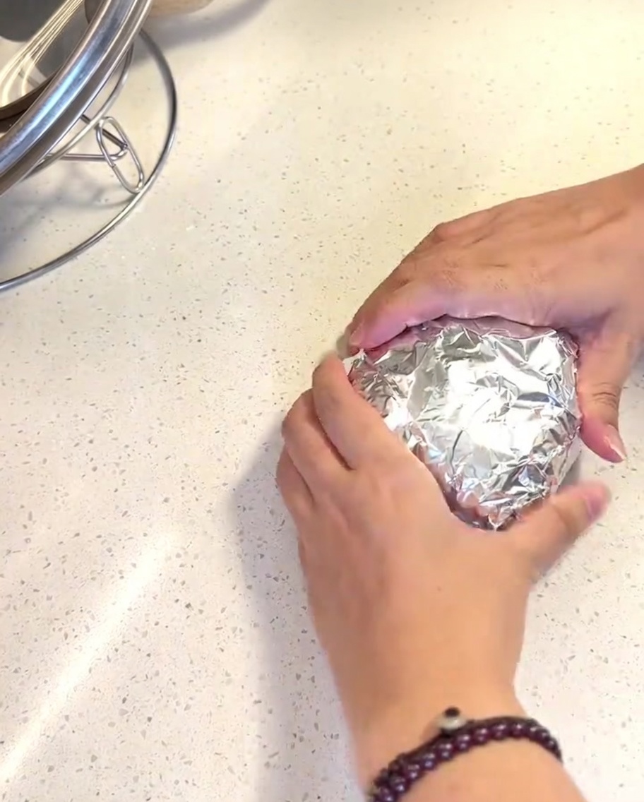 Hamburger buns wrapped in shiny aluminum foil inside the basket of an air fryer.
