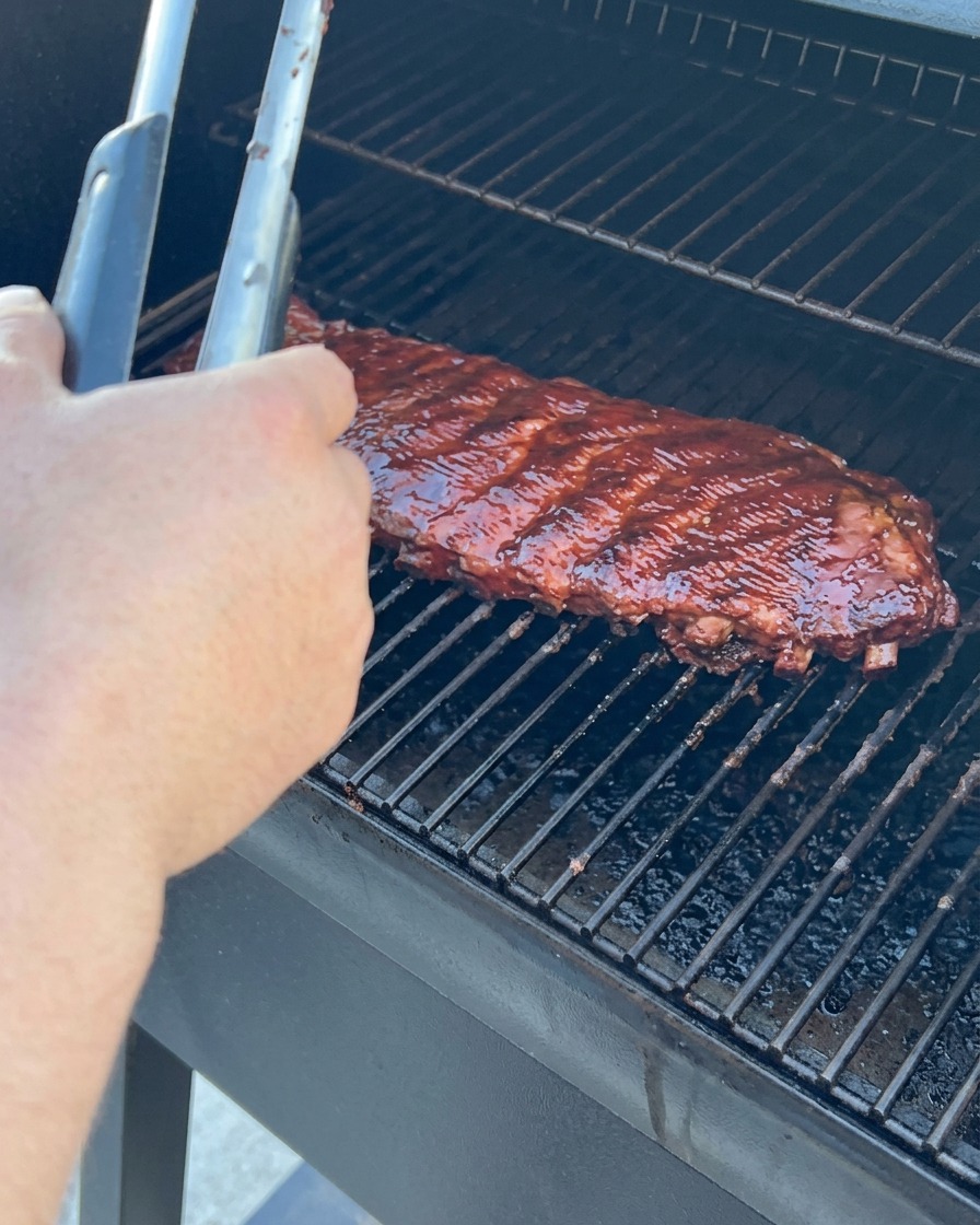 Apple juice being poured over ribs on a sheet of foil before the edges are folded to seal the packet.