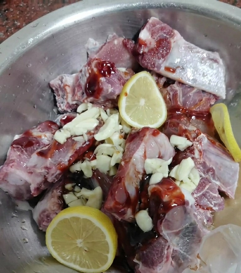 Raw pork ribs mixed with dark marinade, garlic, and fresh lemon slices.