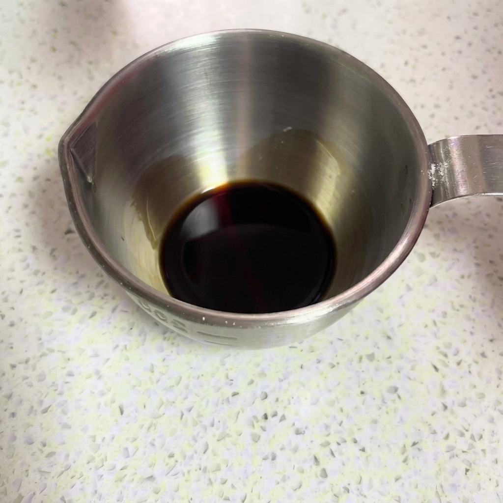 Dark soy sauce being poured into a metal measuring cup.