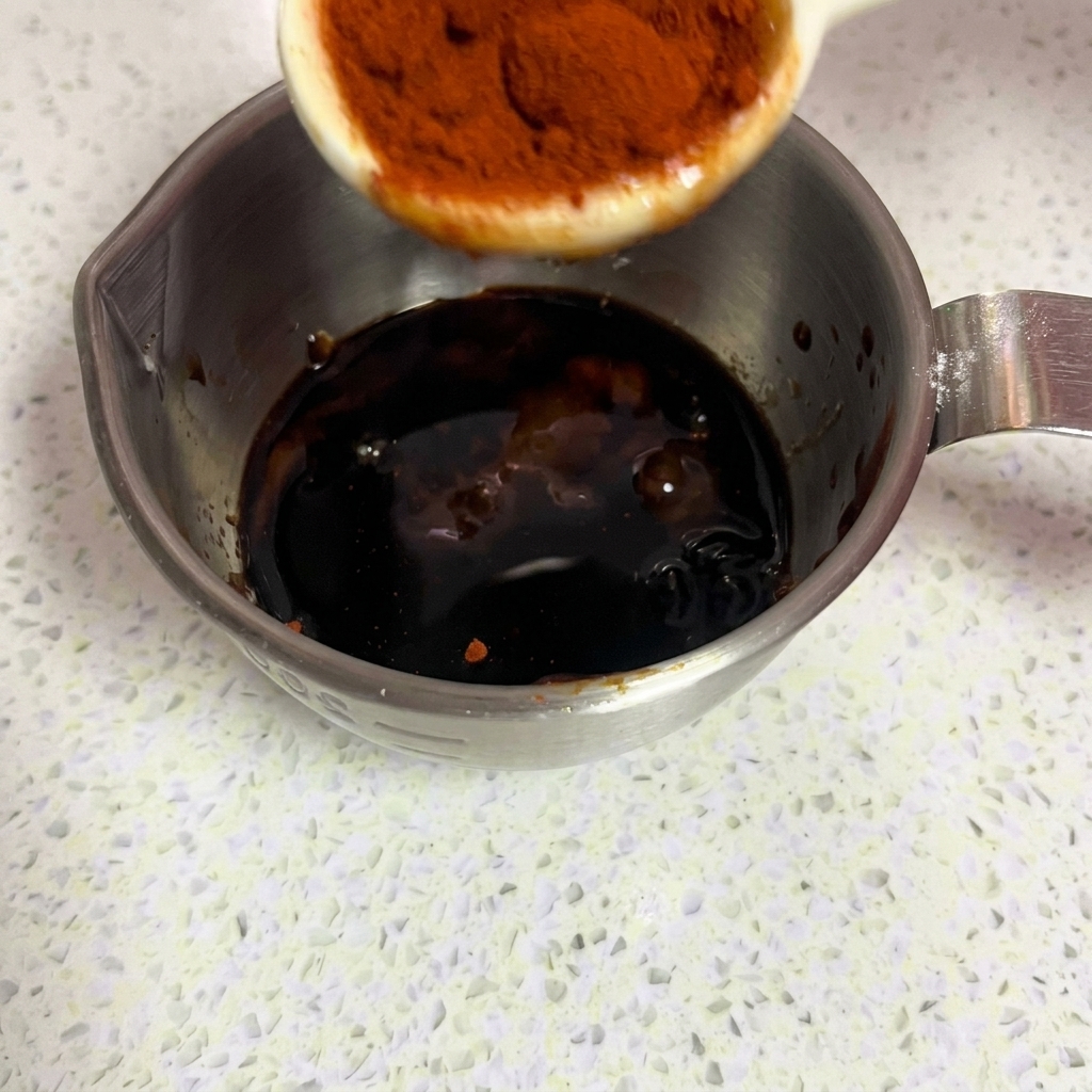 Bright red sweet paprika powder being added to the marinade.