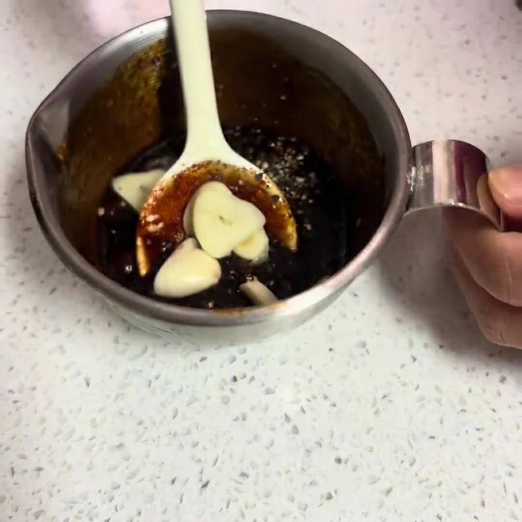 The completed dark, thick marinade with visible fresh garlic slices being stirred.