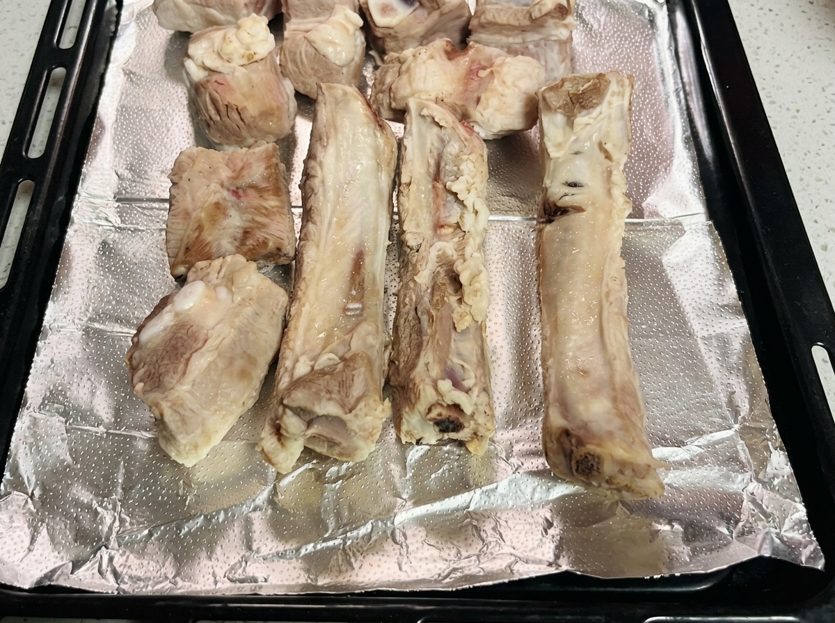 Blanched pork ribs arranged neatly on a foil-lined baking tray.
