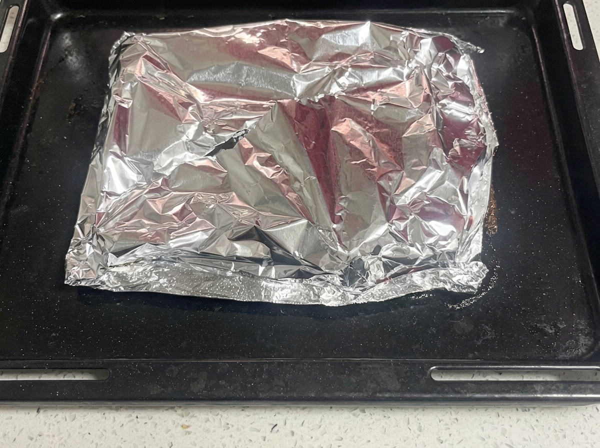 A knife cutting through the top layer of foil to reveal cooked, steaming pork ribs.