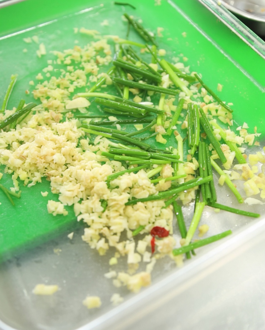 A container filled with fresh minced garlic, vibrant green chopped chives, and a generous dollop of deep red Korean hot pepper paste.