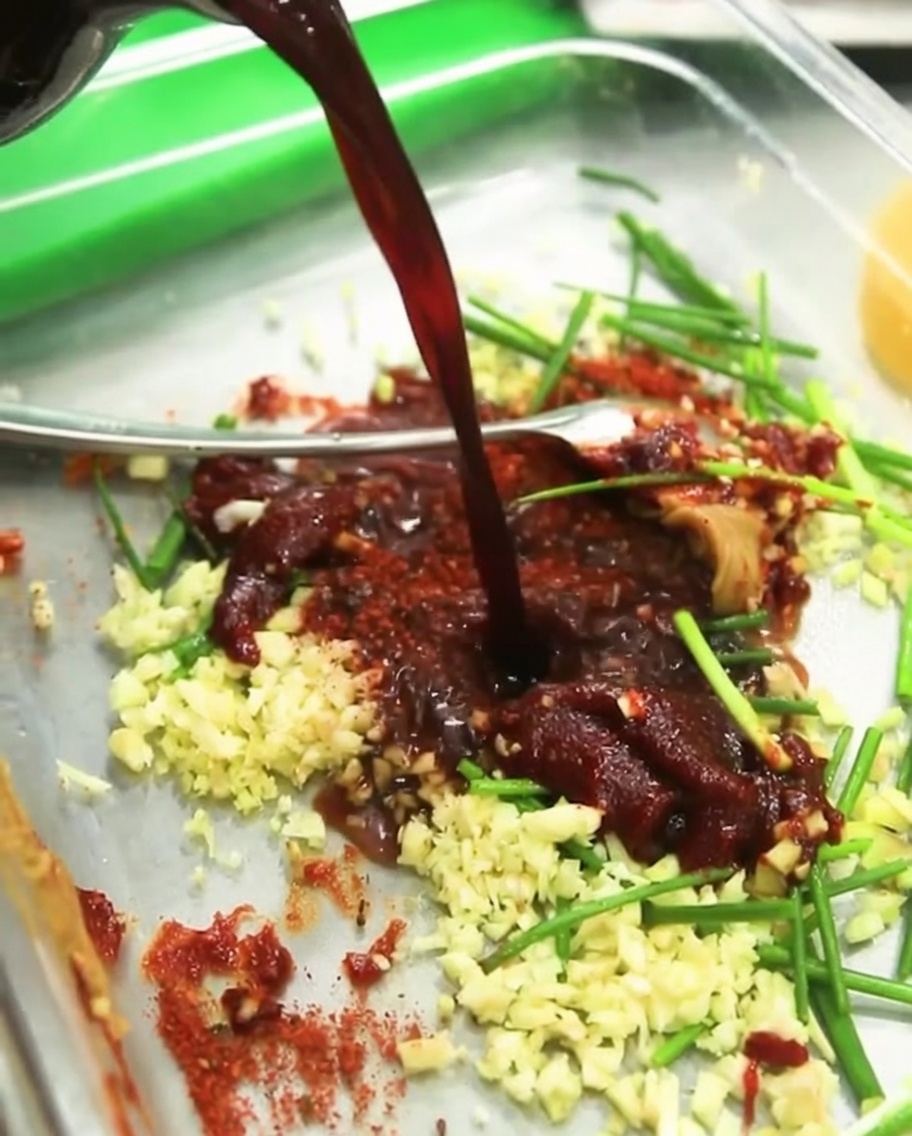 Clear cooking wine being poured into the marinade bowl, blending with the existing soy sauce, peppers, and aromatics.