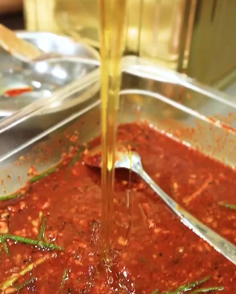 A close-up view of maltose syrup being poured into the red marinade.