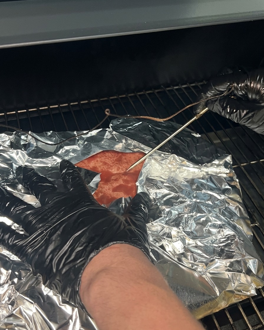 The wrapped brisket placed back onto the smoker grates with the thermometer probe re-inserted.