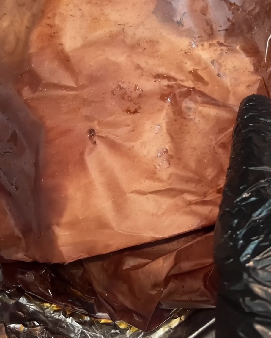 The fully cooked brisket unwrapped, showing a dark, moist bark and rich juices pooling in the butcher paper.