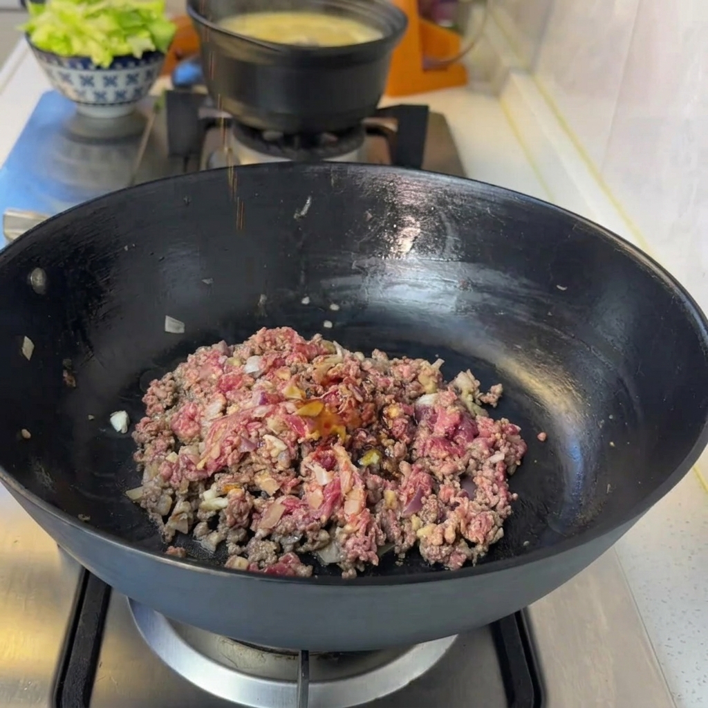 Beef mixture in a pan being seasoned with soy sauce, pepper, and ketchup.