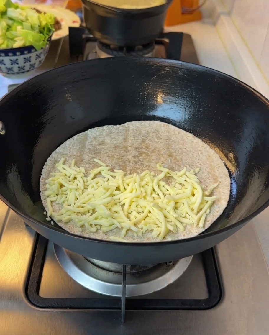 Finely chopped lettuce being added on top of the melted cheese on a tortilla.