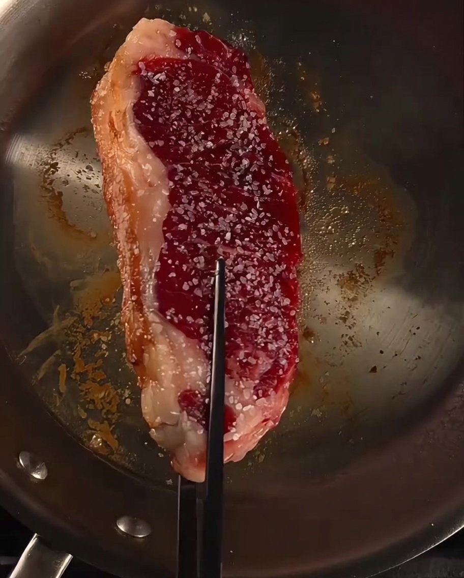 Steak in a pan being basted with butter, garlic, and fresh rosemary sprigs.