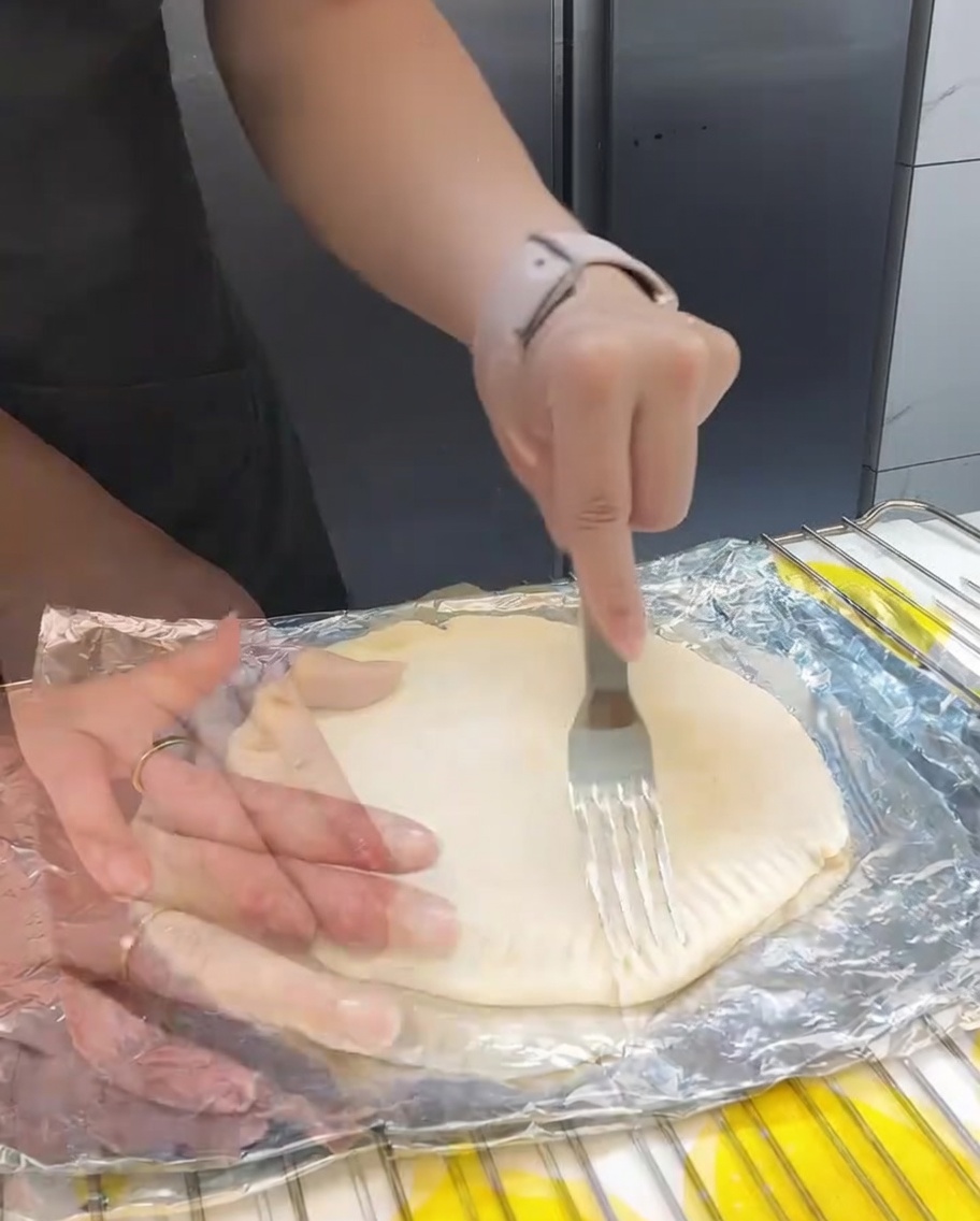 Fork crimping the edges of the stacked scallion pancakes to create a decorative and functional seal.