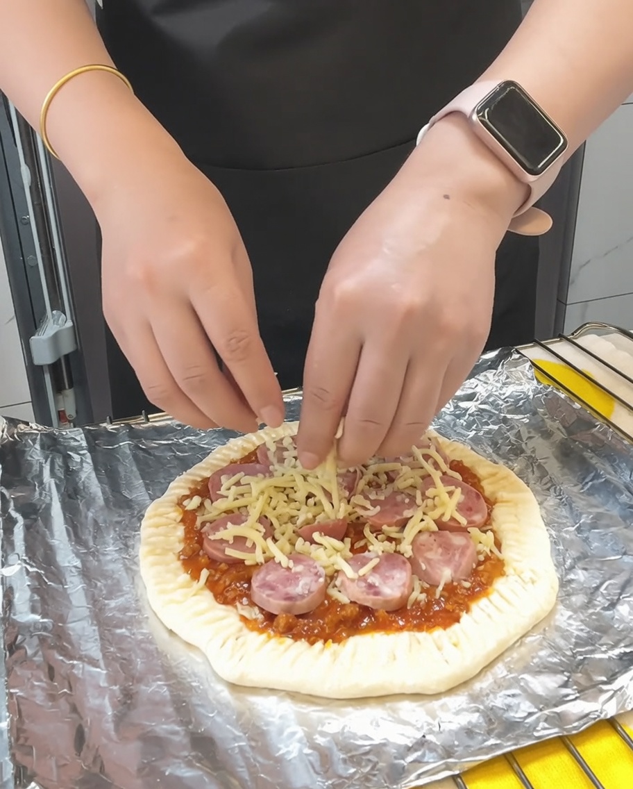 Final handful of mozzarella cheese being scattered over the pizza, followed by a light dusting of dried parsley.