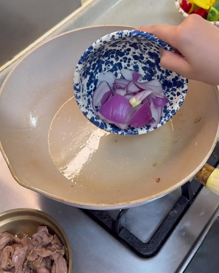 Purple onion pieces being stir-fried in a lightly oiled pan.