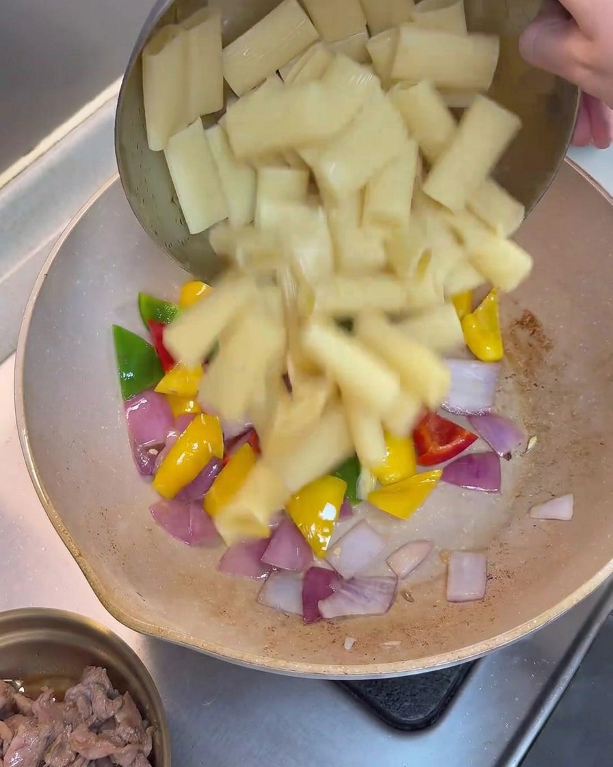 Cooked rigatoni pasta being added to the pan of stir-fried bell peppers and onions.