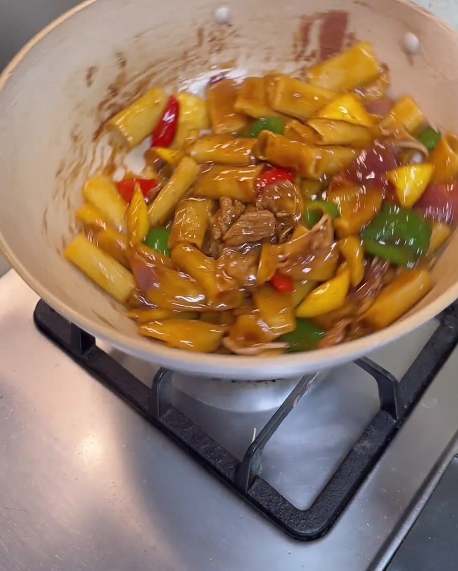 Rigatoni, meat, and vegetables being tossed together in the pan until fully coated in a glossy brown sauce.