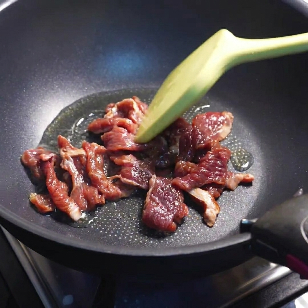 Beef slices browning in a hot pan.