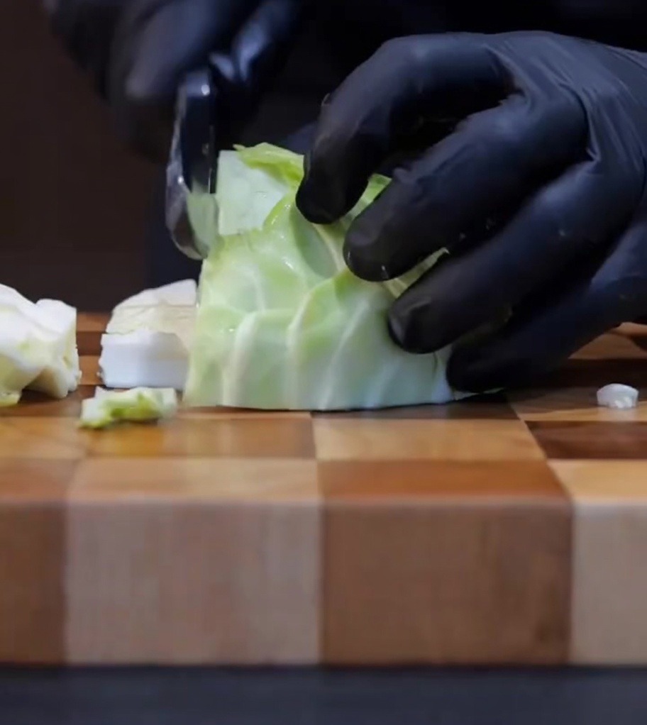 Fresh cabbage being chopped into smaller, bite-sized pieces on a wooden cutting board.