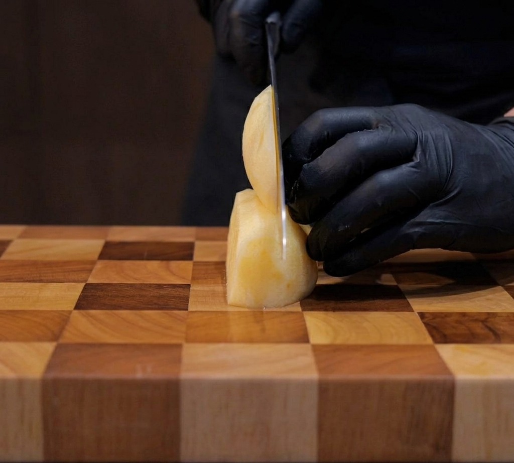 Potatoes being carefully sliced into neat one-centimeter cubes on a wooden cutting board.