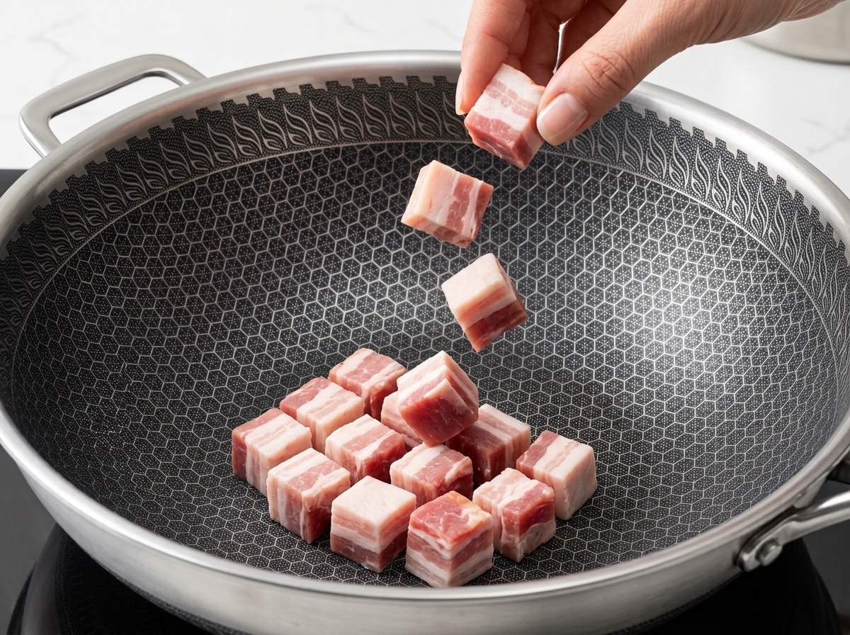 Bacon chunks frying in a pan, turning golden brown with rendered fat at the bottom.