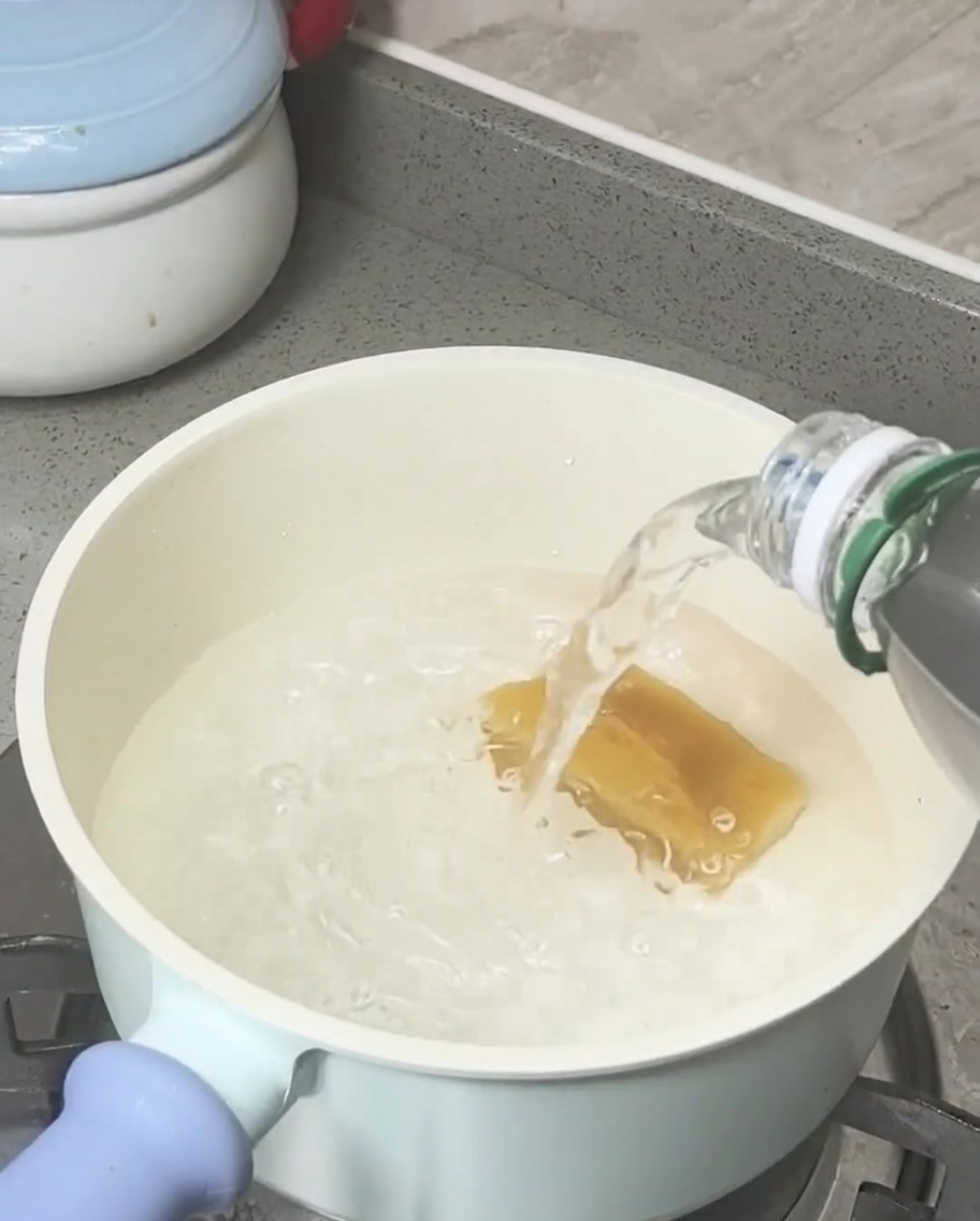 Brown sugar block melting in boiling water in a light-colored pot.