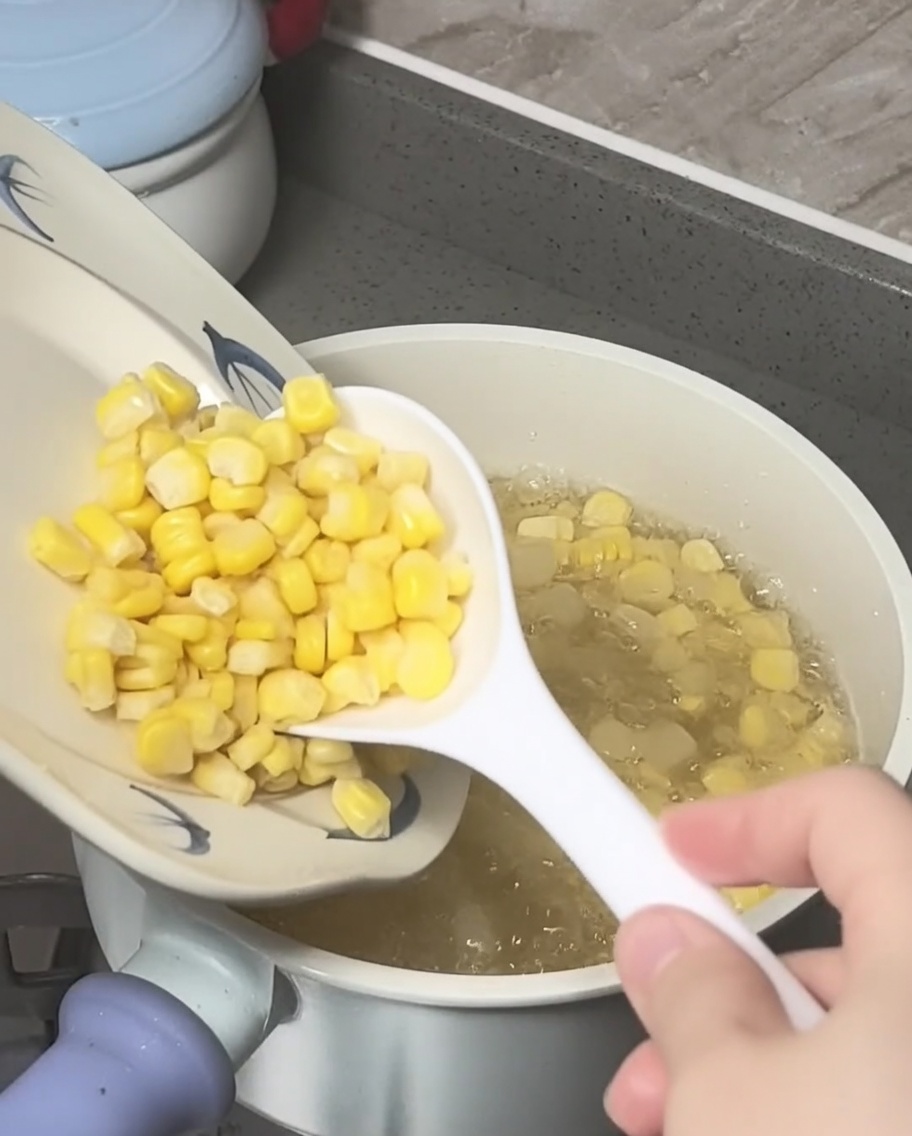 Corn kernels and crushed water chestnuts being added to a boiling pot of sugar water.