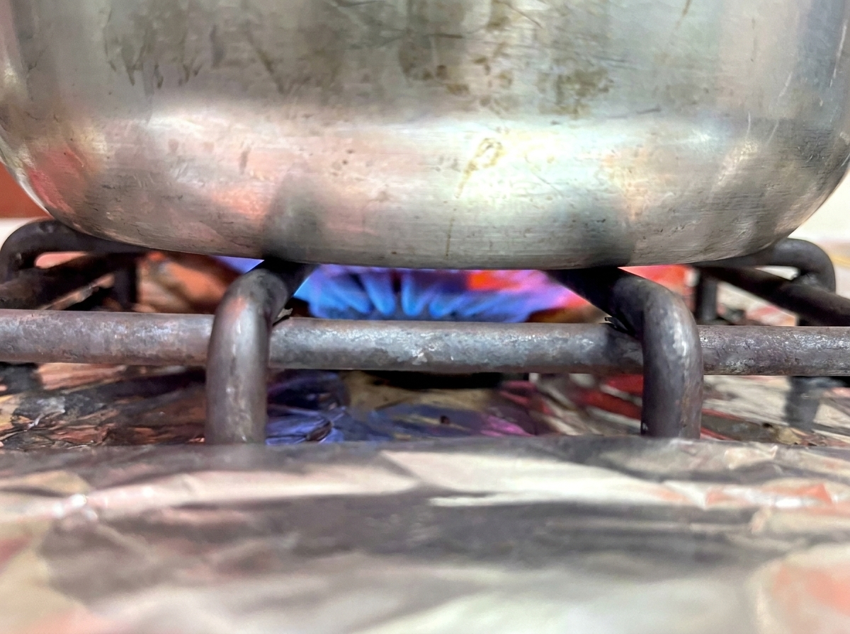 The bottom of a metal pot resting on a gas stove burner with a blue flame underneath.