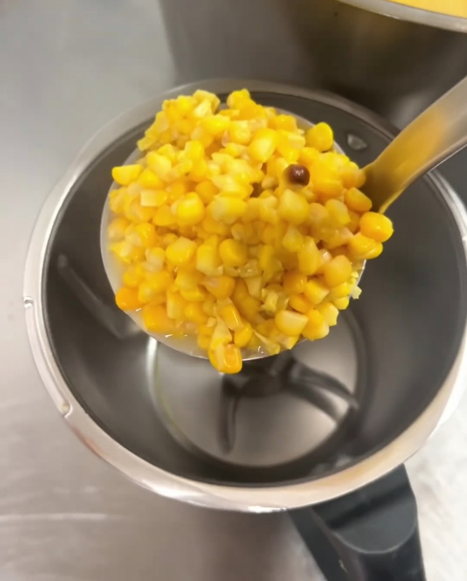 Cooked corn kernels being added into a large blender jar.