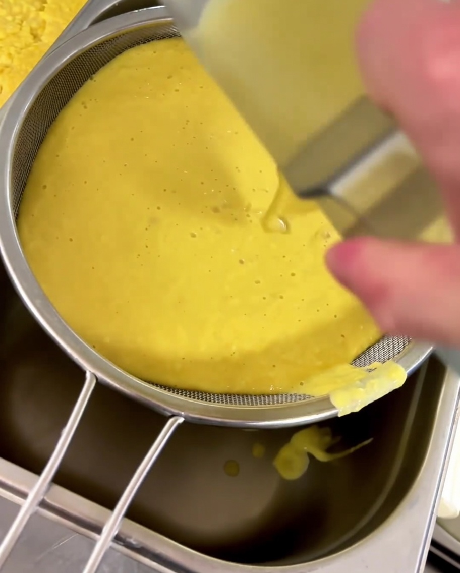 Yellow corn soup being strained through a fine-mesh sieve into a container.