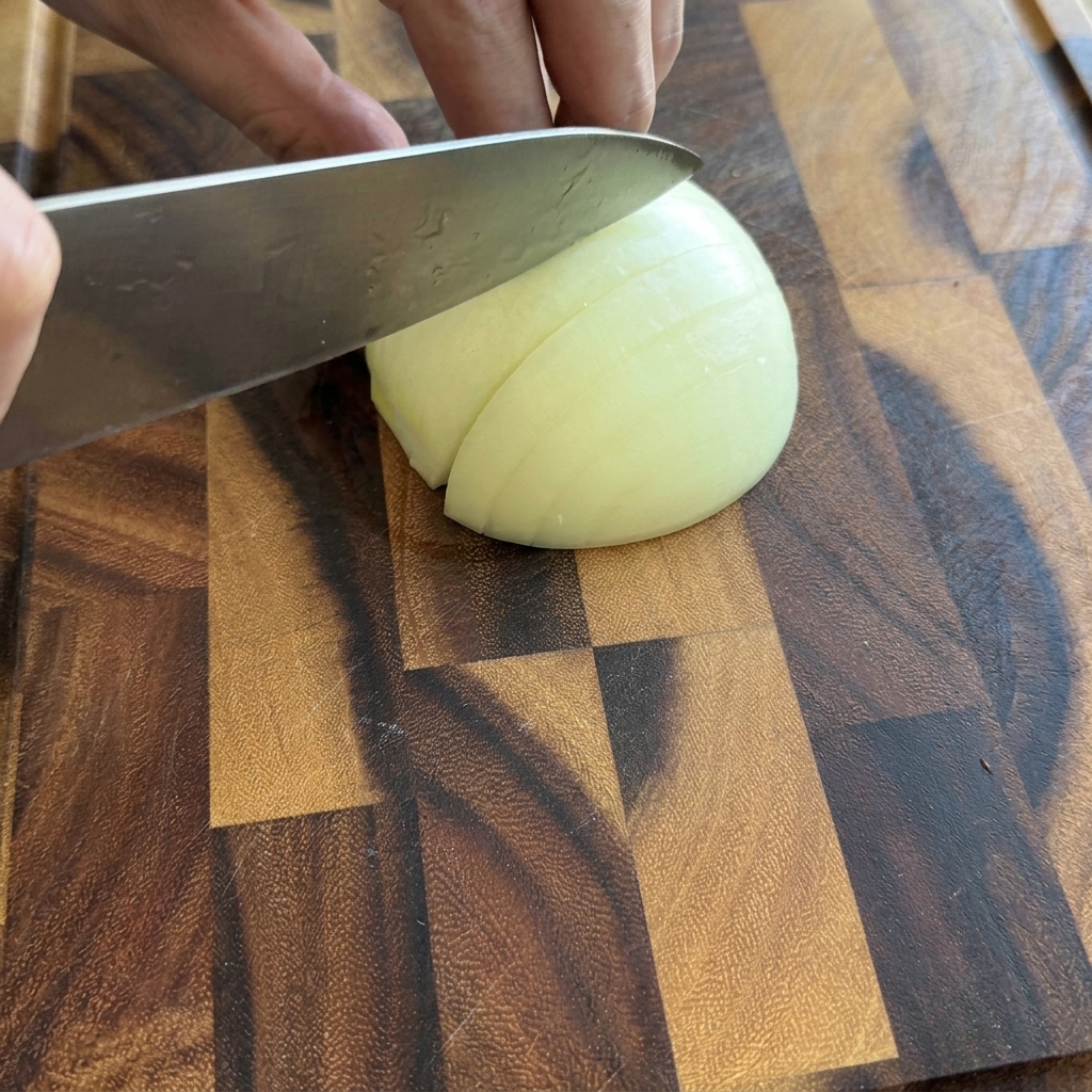 A person slicing a white onion half into small diced pieces on a wooden cutting board.