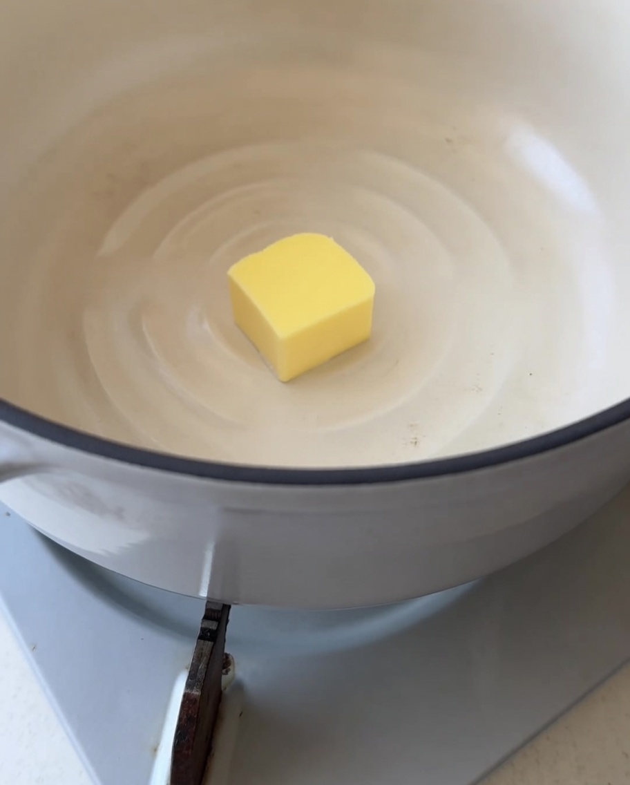 Close-up of a single square of yellow butter starting to melt in a clean white pot.