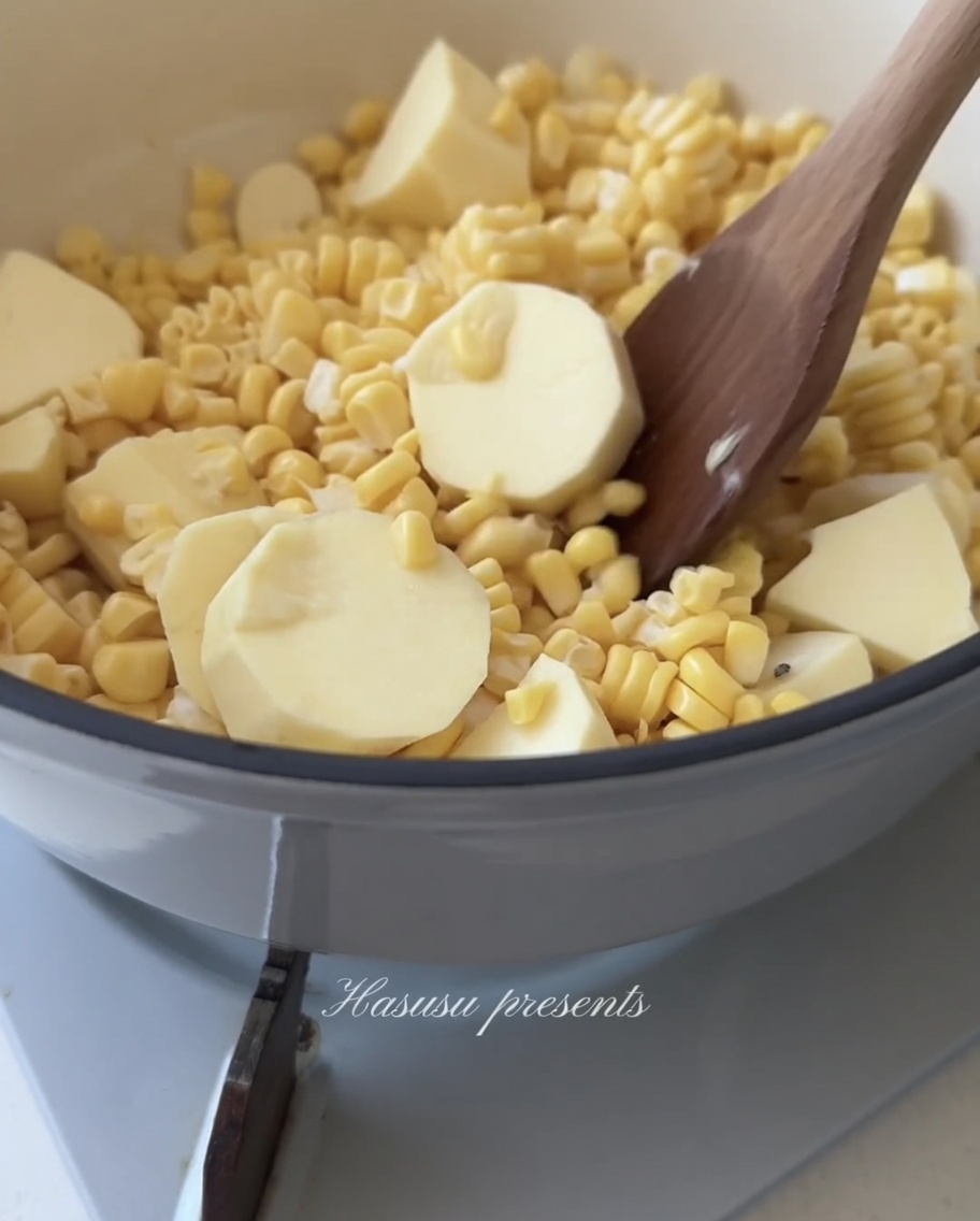 A wooden spoon stirring a mix of yellow corn kernels and white sweet potato chunks in a pot.