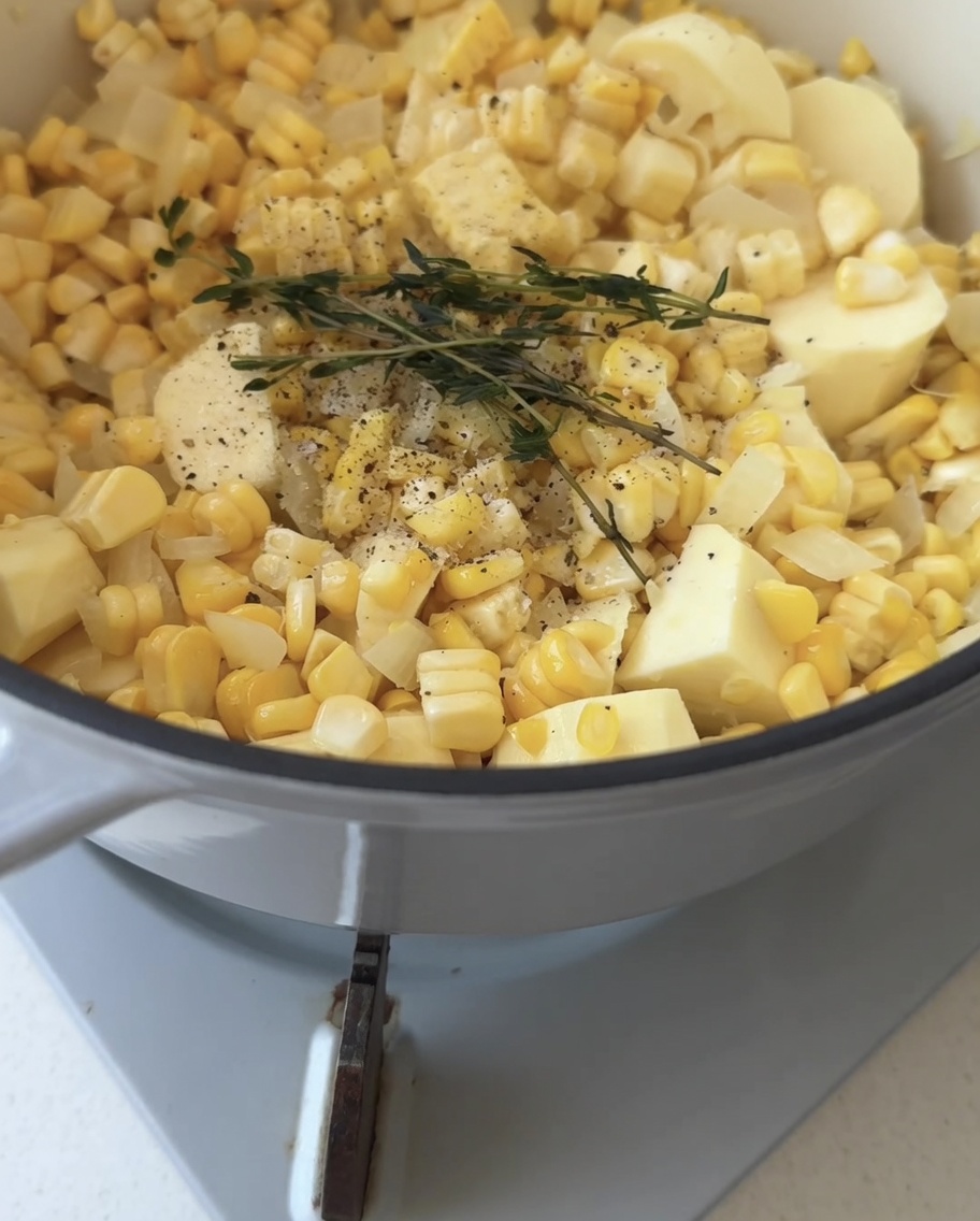 Clear water being poured into a pot over vegetables and a single green sprig of thyme.