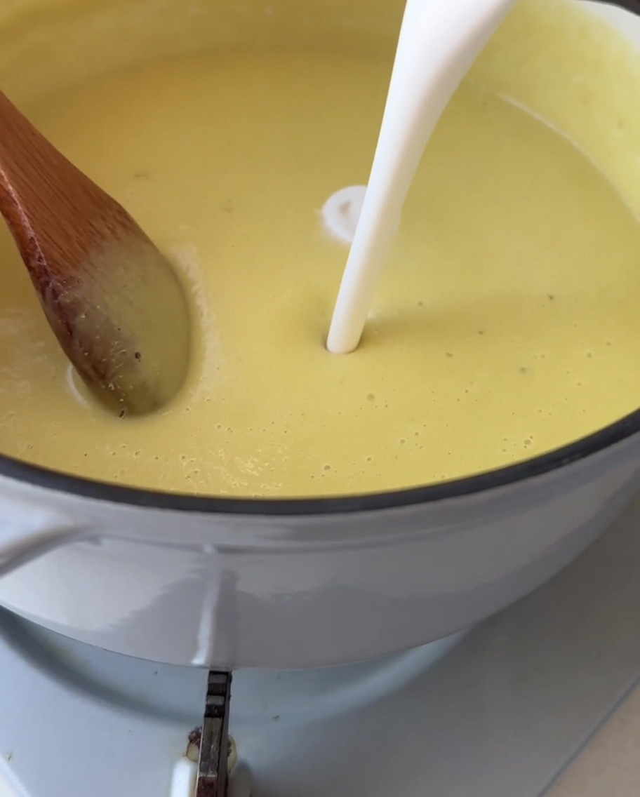 White cream being poured into a pot of smooth, bright yellow corn soup.