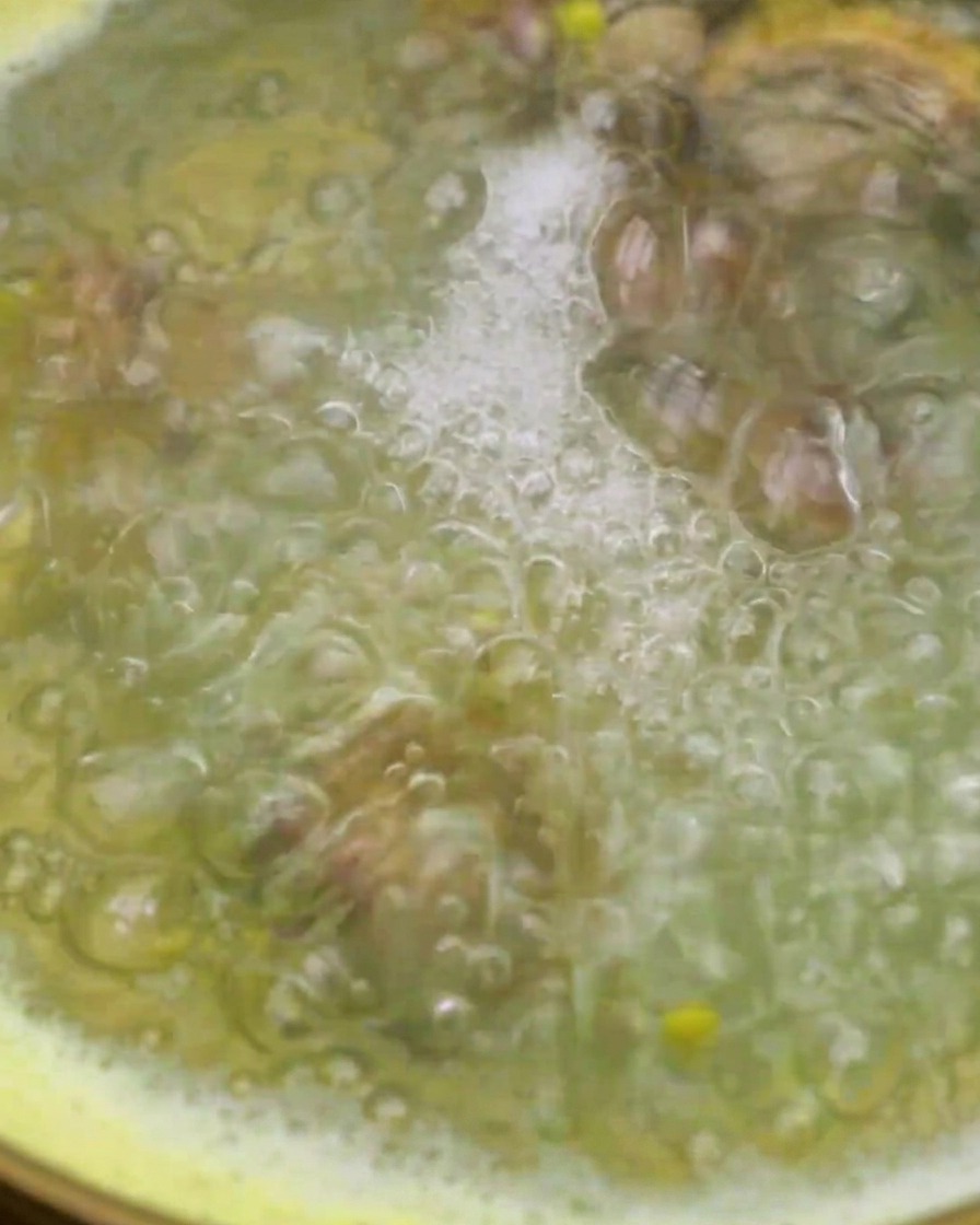 Clams being added into a pot of boiling corn water using a mesh strainer.