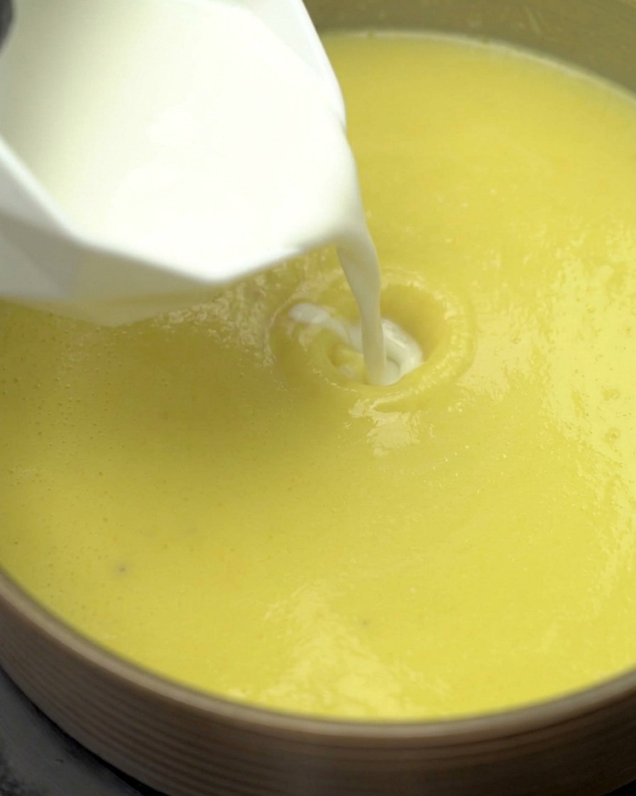 Milk and light cream being poured into the simmering corn soup base in a pot.