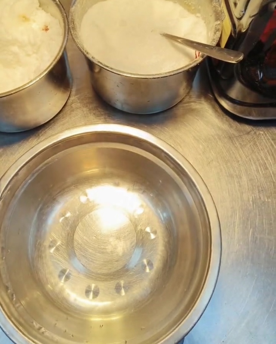 Multiple small metal containers filled with various white granular and liquid seasonings on a prep table.