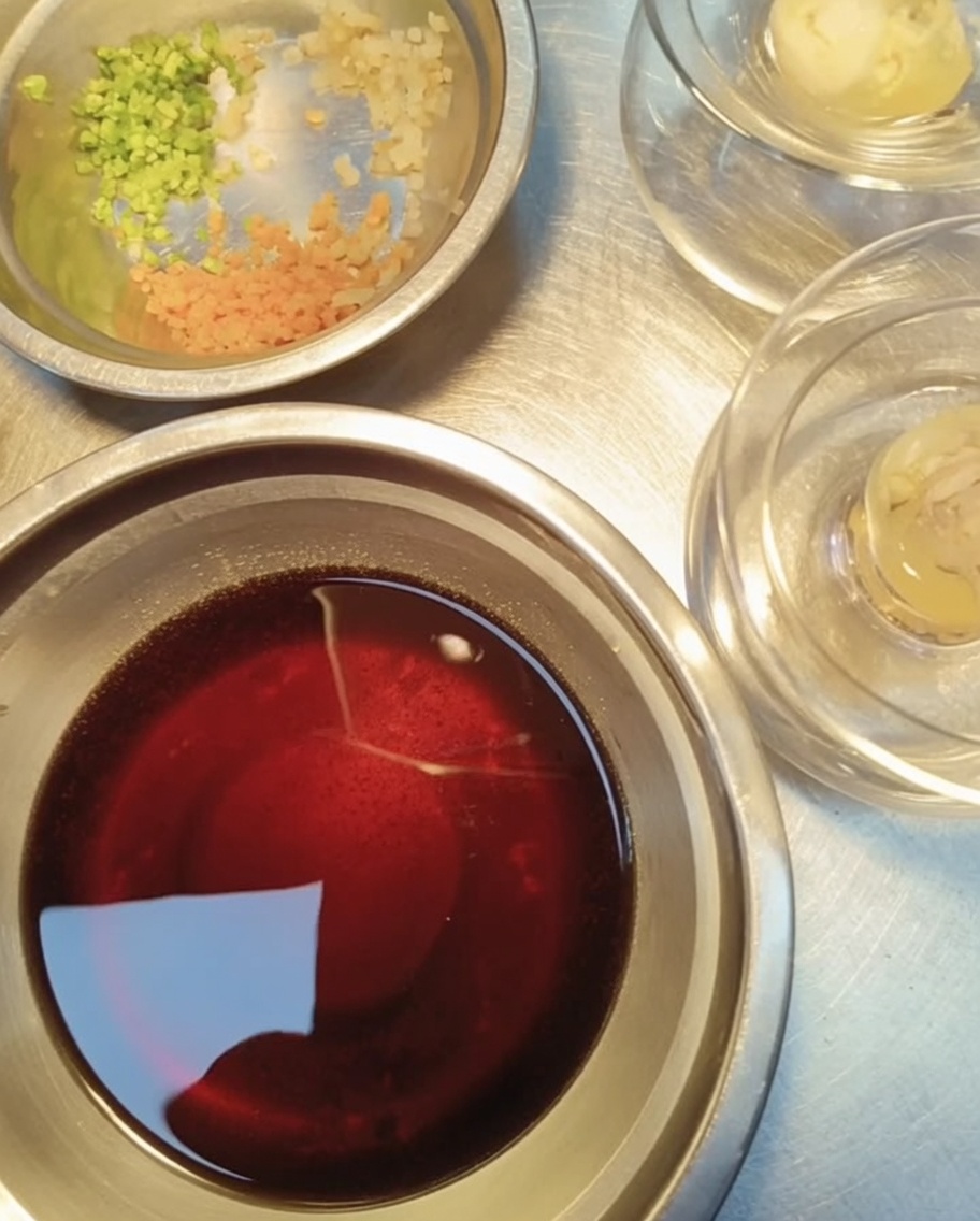 Close-up view of small metal containers holding freshly minced garlic, finely chopped cilantro, and diced carrots, prepared for garnishing the seafood jelly.