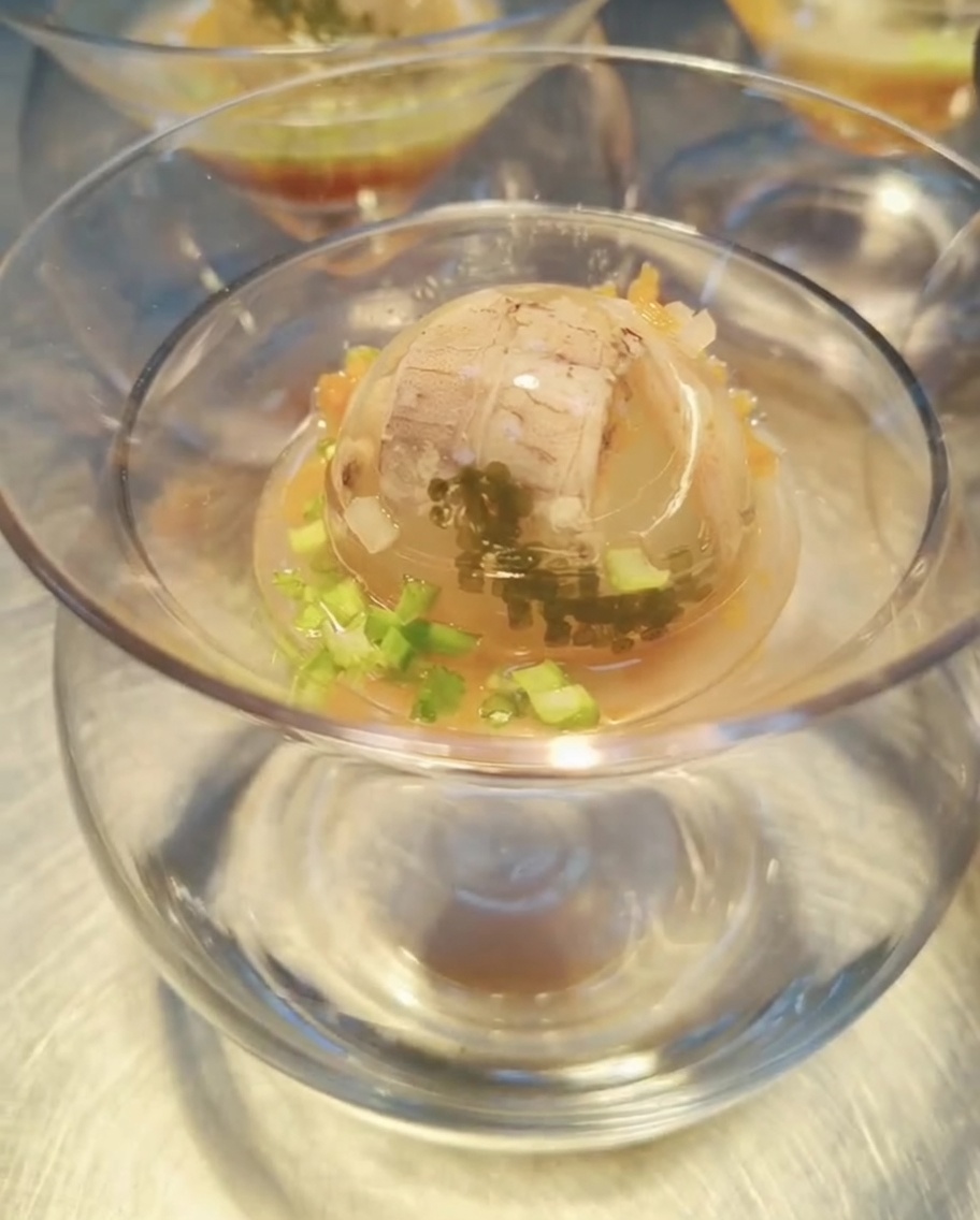 A perfectly set seafood jelly sphere in a glass bowl, being drizzled with a rich amber sauce, ready to be garnished and served.