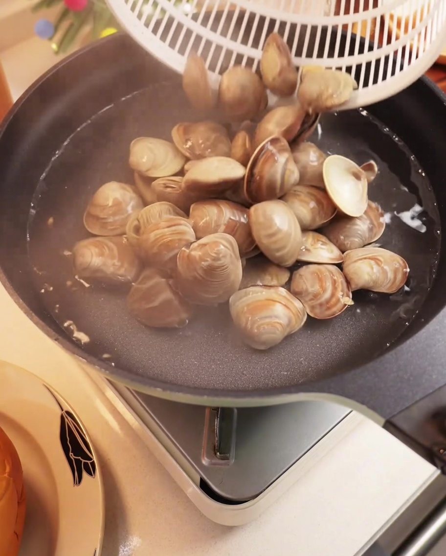Fresh clams boiling in a pot with water, shells opening.