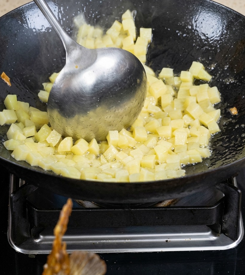 Diced potatoes being sautéed in a wok with oil until lightly browned.