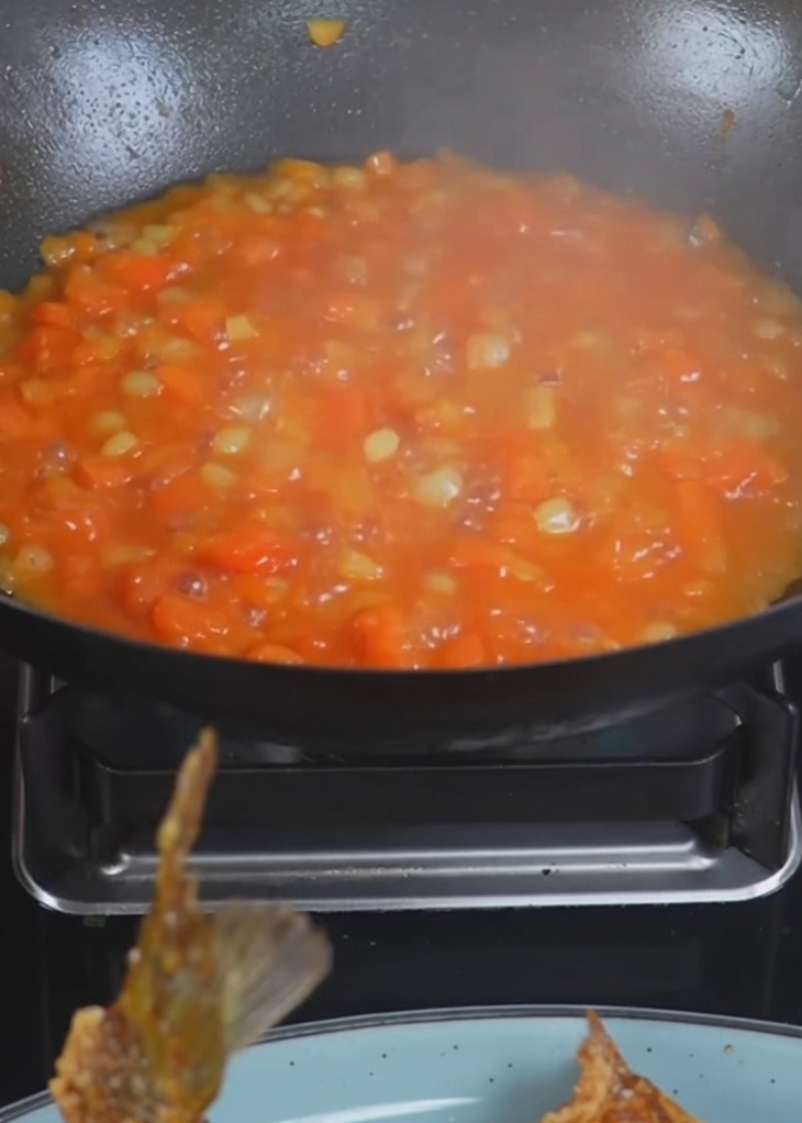 Boiling water being poured into a wok containing cooked potatoes and tomatoes.
