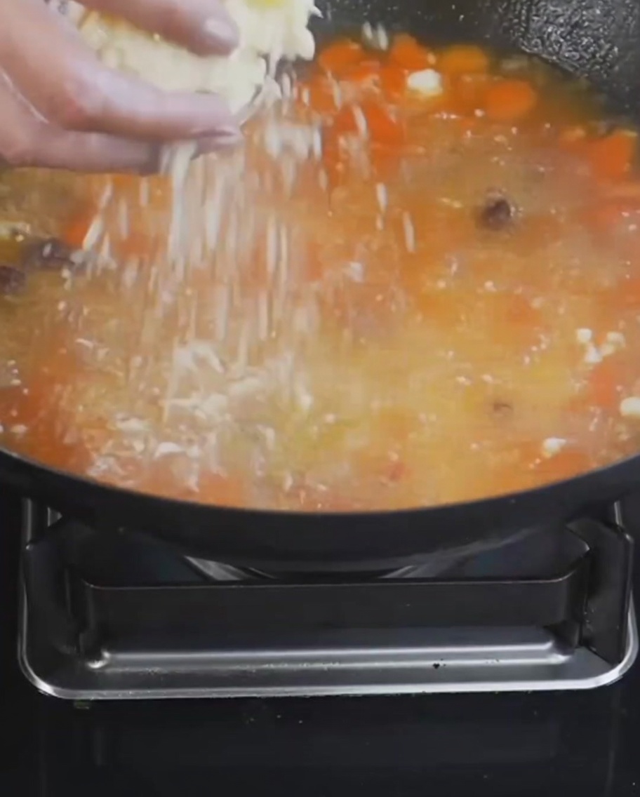 Flour and egg nuggets being sprinkled into a simmering pot of soup with tomatoes and potatoes.