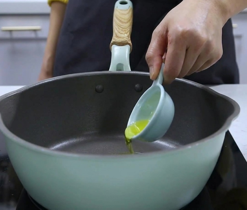 Pouring walnut oil from a small measuring spoon into a cooking pot.