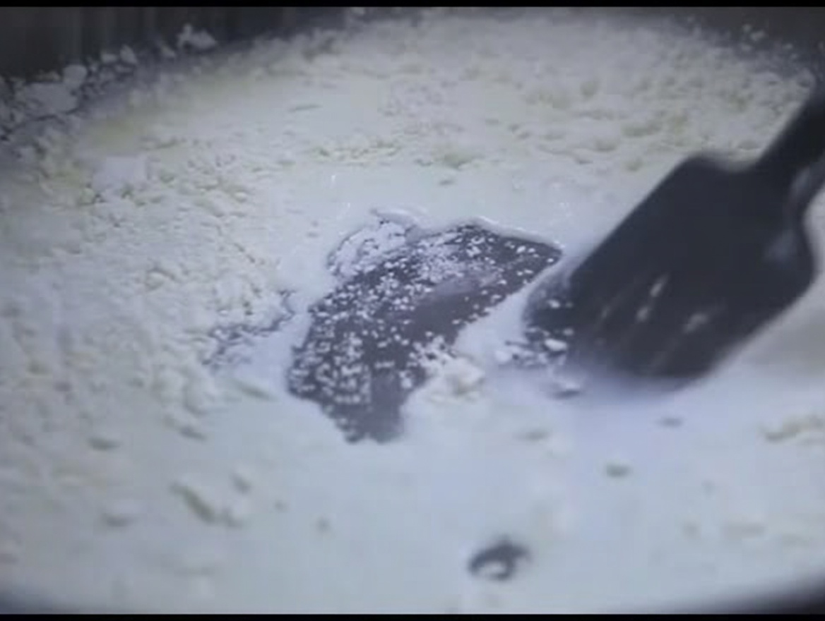 A black silicone spatula stirring a thick, white milk and flour mixture in a pan.