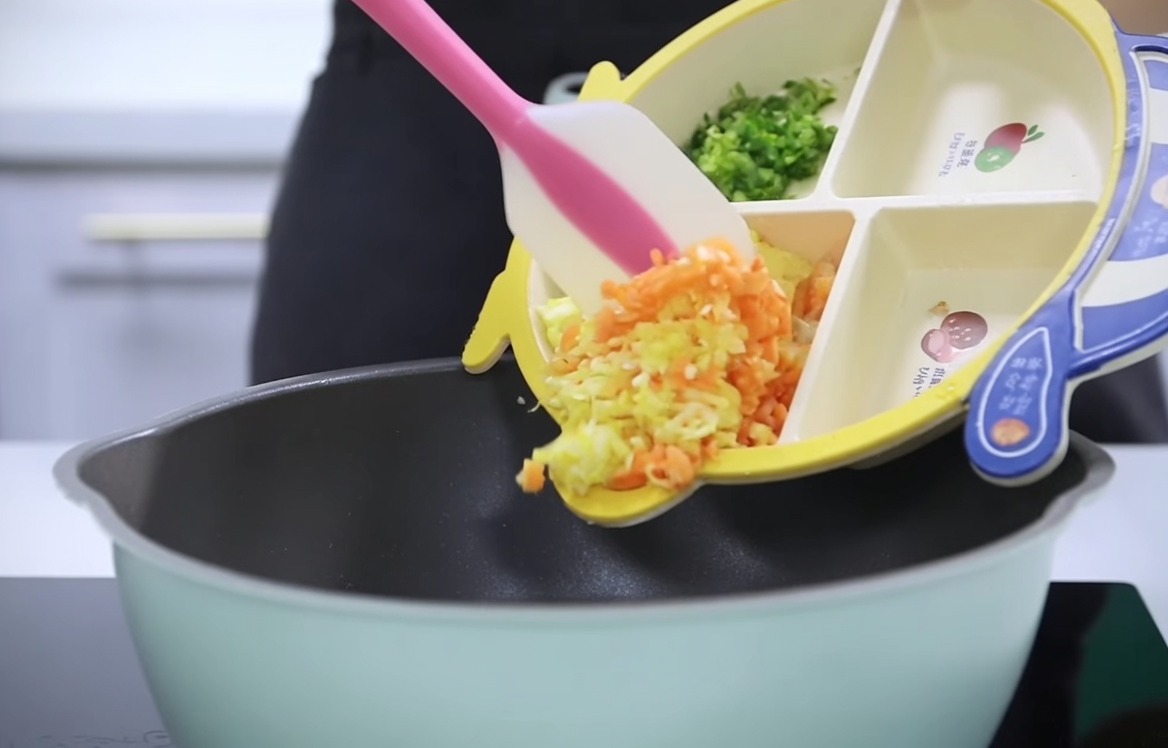 Chopped carrots, potatoes, and celery being poured from a segmented baby plate into a pot.