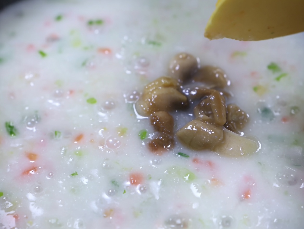 Cooked clam meat being added to a simmering, creamy vegetable soup.